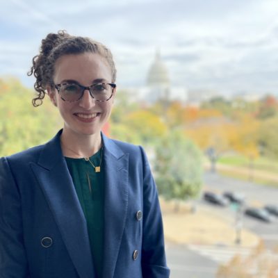 Caitlin Ballotta Rajagopalan is smiling and wearing a blue blazer and glasses.