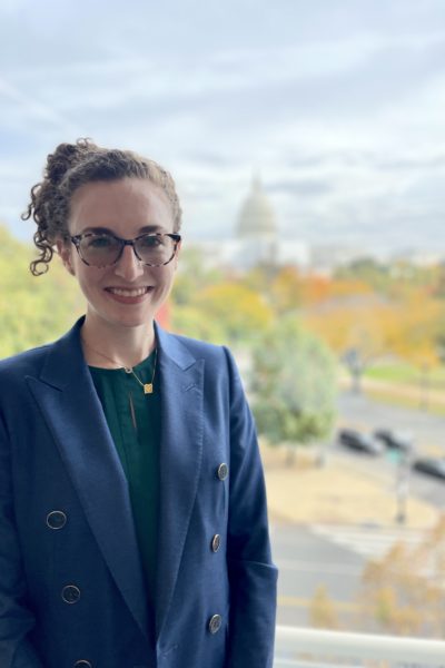 Caitlin Ballotta Rajagopalan is smiling and wearing a blue blazer and glasses.