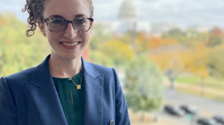 Caitlin Ballotta Rajagopalan is smiling and wearing a blue blazer and glasses.