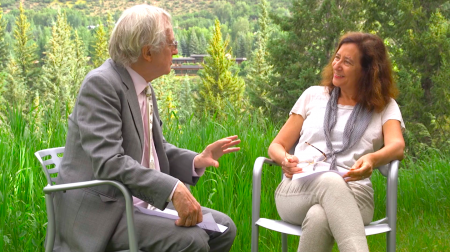 Richard Dawkins, clad in a gray suit, is seated and gesturing with his left hand while engaged in conversation with Elisa New.