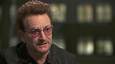 Portrait of singer-songwriter Bono wearing pink-tinted glasses and a suit.