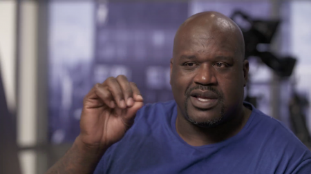 Portrait of Shaquille O'Neal wearing a blue shirt, hands gesturing, and in mid-speech.