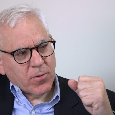 Portrait of David Rubenstein gesturing with hands and in mid-speech.