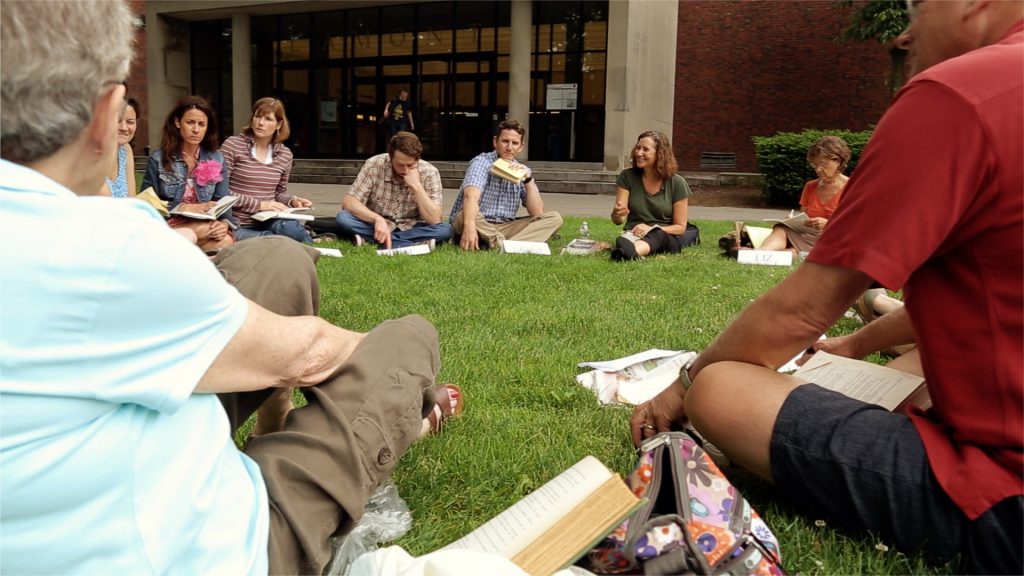 Elisa New sits on a lawn in a circle with several teachers.