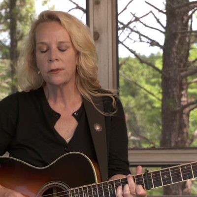 Mary Chapin Carpenter, wearing a black top and playing the guitar