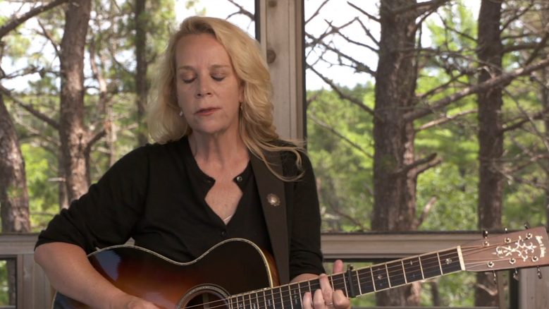 Mary Chapin Carpenter, wearing a black top and playing the guitar