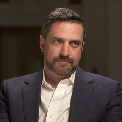 Portrait of Raul Esparza wearing a suit and looking off to the side.
