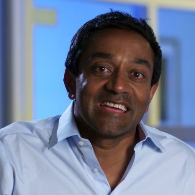 Portrait of M. Sanjayan wearing a blue button-up shirt and smiling