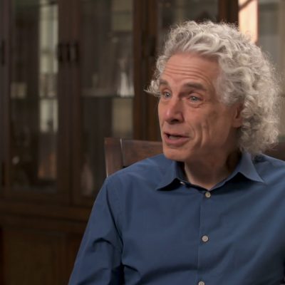 Portrait of Steven Pinker wearing a blue button-up shirt and in mid-speech.