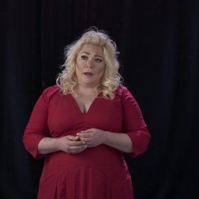 Opera singer Amanda Zory in a red dress, hands below chest, captured mid-song.