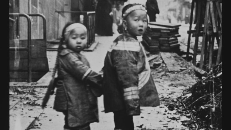 Black and white photograph of two children holding hands and looking back over their shoulders at the photographer, taken in Chinatown, San Francisco sometime between 1895 and 1906.