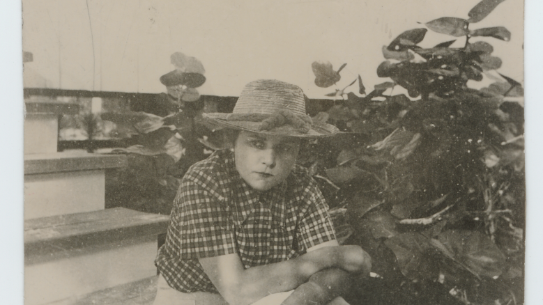 Elizabeth Bishop portrayed seated on steps, wearing a hat with hands folded in her lap.