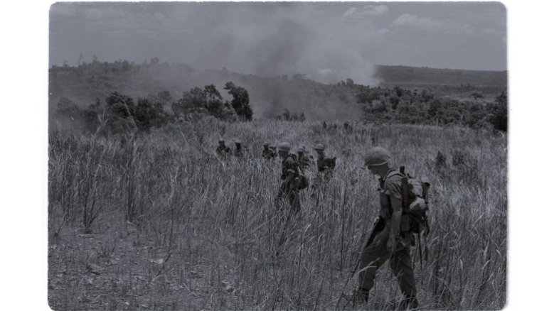 Black and white photograph of Marines walking through burned rice patties