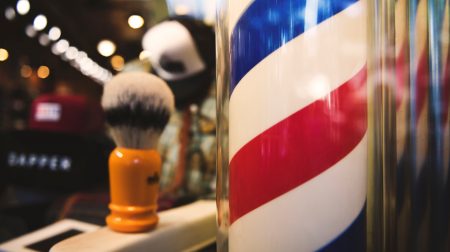 A classic barber pole with red, white, and blue stripes spiraling around it.