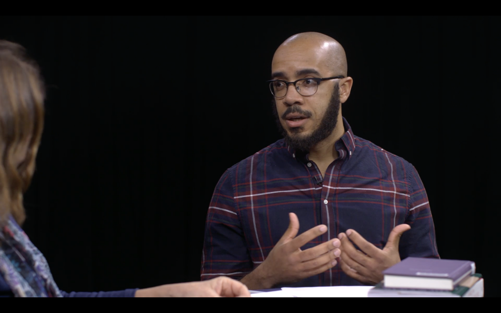 Clint Smith in a collared shirt, sitting and chatting, hands in motion.