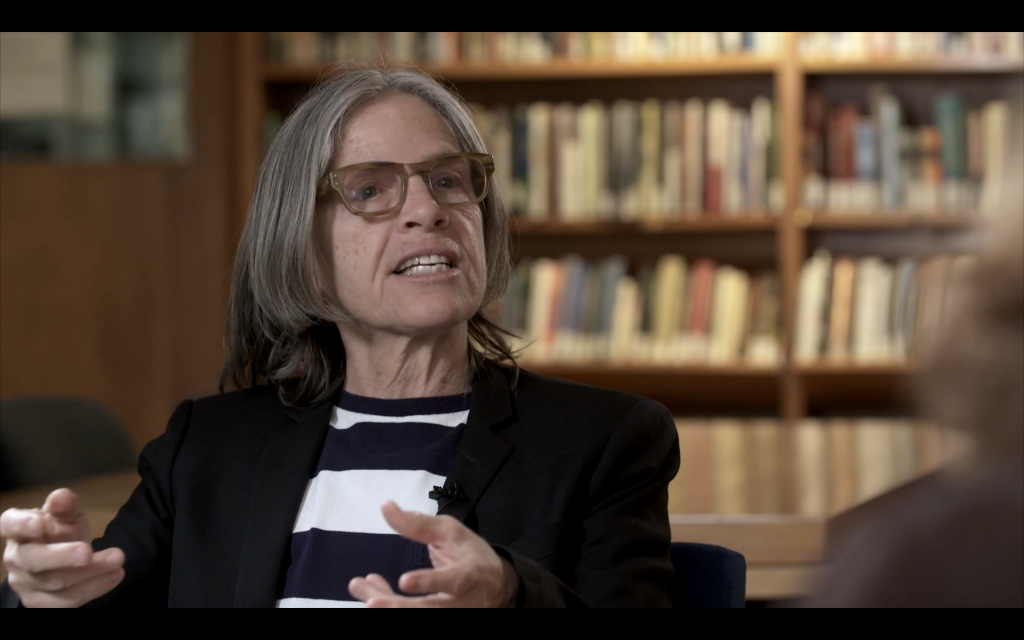 Eileen Myles in the middle of speaking with hands in the middle of gesturing.