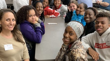 A group of students sitting around a table looking up and smiling.