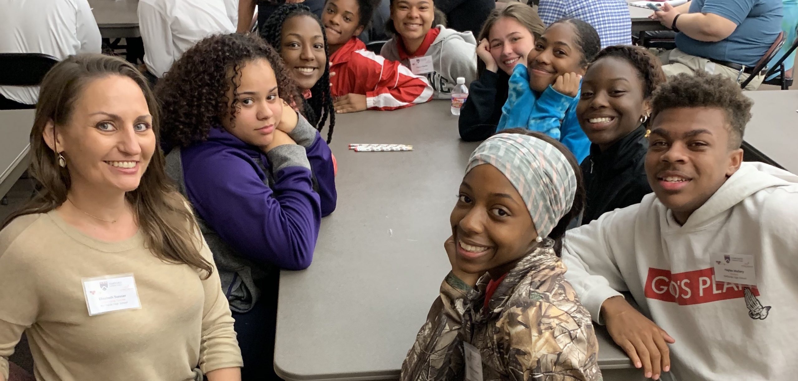 A group of students sitting around a table looking up and smiling.