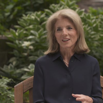 Caroline Kennedy, wearing a black long-sleeved collared shirt, in the middle of speaking.