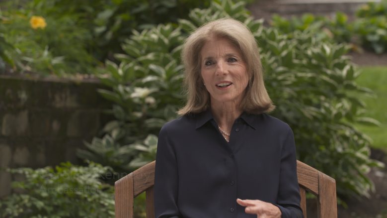 Caroline Kennedy, wearing a black long-sleeved collared shirt, in the middle of speaking.