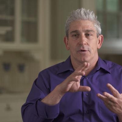 Richard Blanco, wearing a purple shirt, gestures with his hands whilst he speaks.