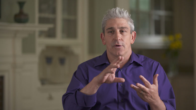 Richard Blanco, wearing a purple shirt, gestures with his hands whilst he speaks.