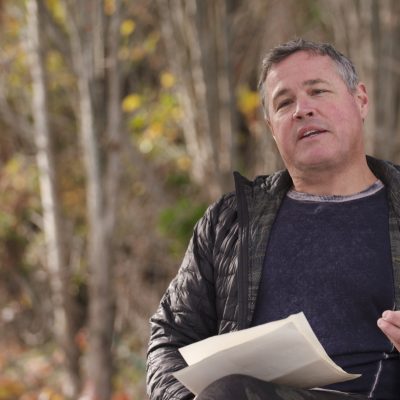 Jeff Corwin, wearing a black jacket, in the middle of speaking while gesturing with his left hand and holding paper in his right hand.
