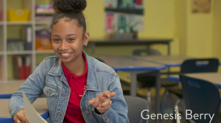 Student Genesis Berry, wearing a jean jacket and red shirt, smiles while in the middle of gesturing with her hand.