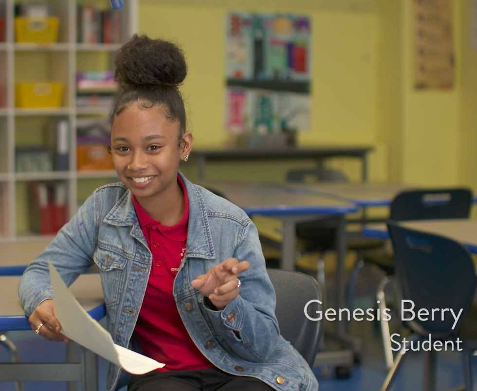 Student Genesis Berry, wearing a jean jacket and red shirt, smiles while in the middle of gesturing with her hand.