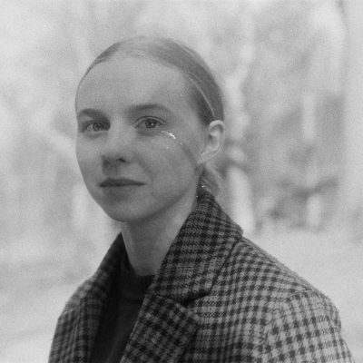 Black and white portrait of Elinor Hitt wearing plaid coat and smiling.