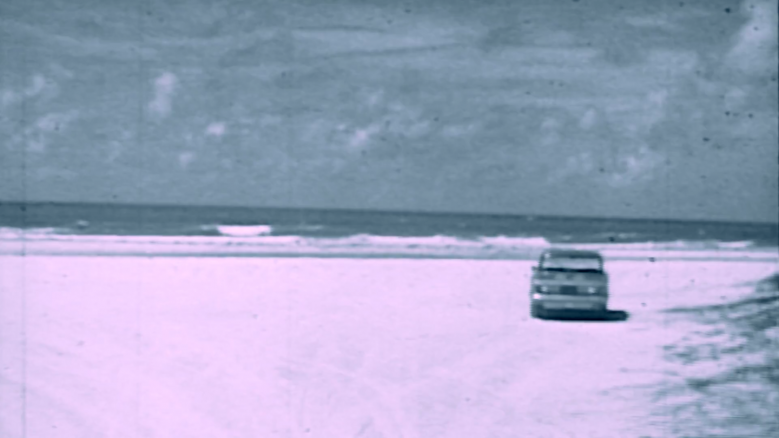 Photograph of a car driving on the beach.