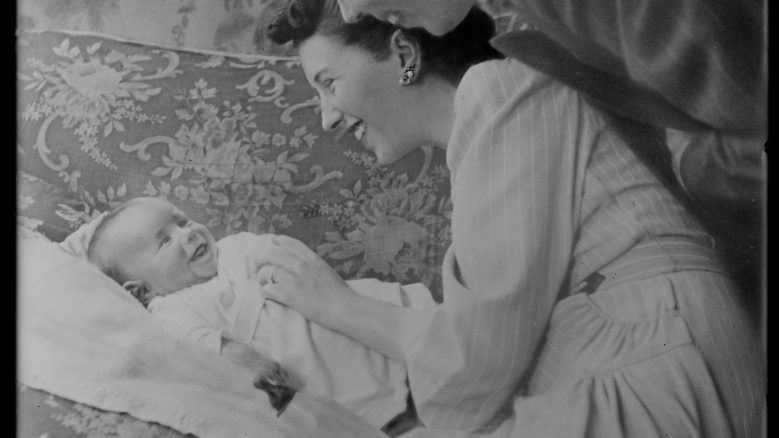 Black and white photo of two parents smiling over a laughing infant.