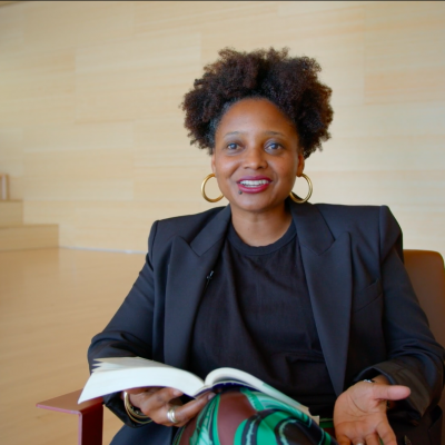 Poet Tracy K. Smith, wearing a black suit, holds a book in her hand while in the middle of speaking.