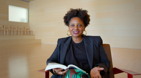 Poet Tracy K. Smith, wearing a black suit, holds a book in her hand while in the middle of speaking.