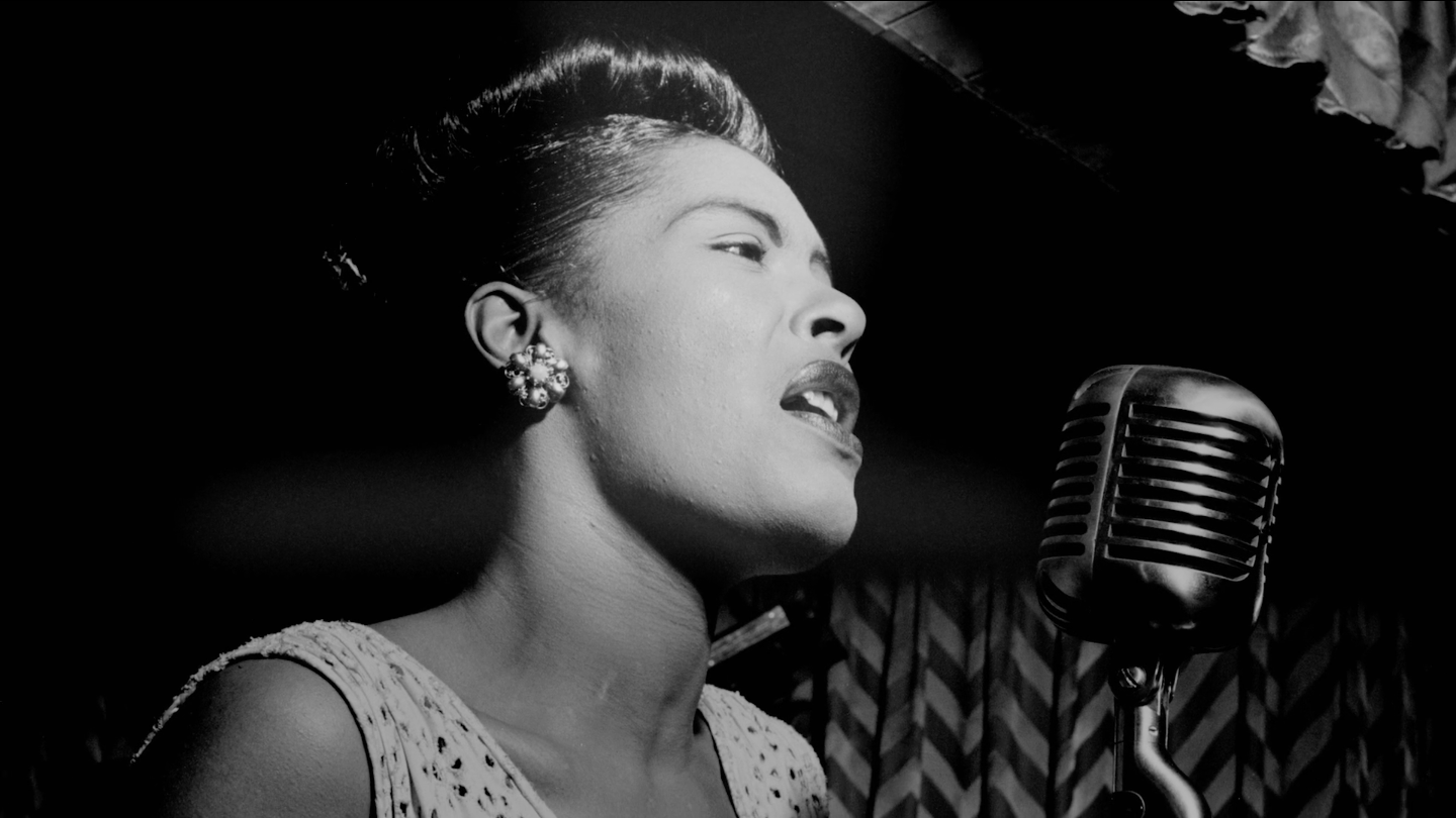 Black and white portrait of American jazz singer and songwriter Billie Holiday singing into a microphone.