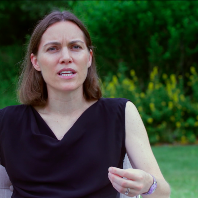 Emily Oster, wearing a back top, in the middle of speaking while gesturing with her left hand.