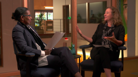 Activist Ayaan Hirsi Ali and host Elisa New sit facing each other. Elisa is gesturing while in the middle of speaking, and Ayaan holds a paper while looking at Elisa.