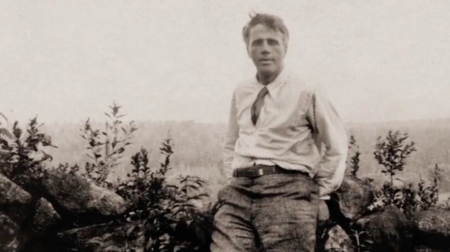 Black and white photo of Robert Frost posing against a landscape