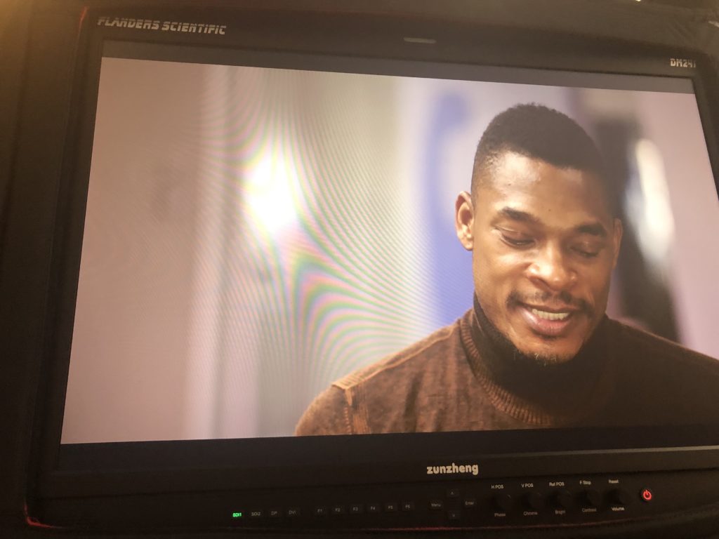 Portrait of poet Terrance Hayes, wearing a brown turtleneck and looking downward, on a camera screen.