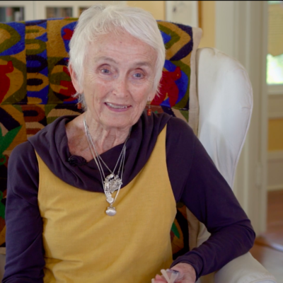 Beverly Lowry smiles while wearing a purple and yellow long-sleeved shirt.