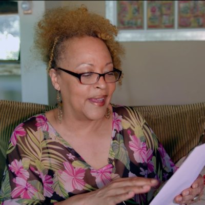 Cassandra Wilson wearing a floral blouse, in the middle of reading from a paper in her hands