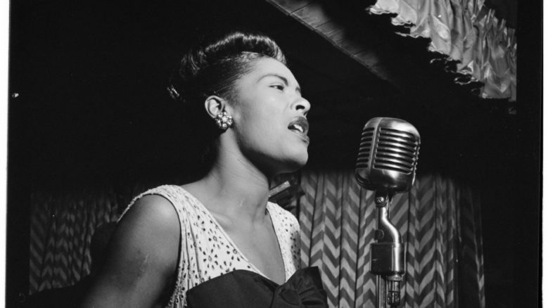 Black and white portrait of American jazz singer and songwriter Billie Holiday singing into a microphone