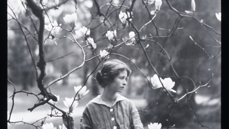 Black and white portrait of Edna St. Vincent Millay holding flowering tree branches and looking to the side