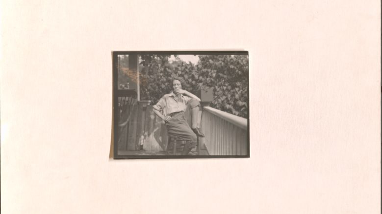 Black and white image of Edna St. Vincent Millay sitting on a chair with a leg propped up and smoking a cigarette