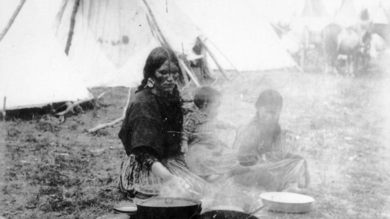 An Indigenous woman with two children sitting on the ground