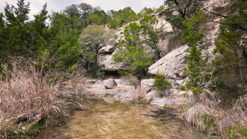 A rocky landscape with trees, shrubs and a pool of water in Texas.