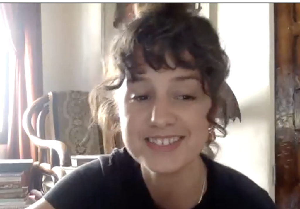 Olivia Gatwood, who has curly brown hair and wears a black top, smiles as she makes the keynote speech at the virtual graduation.