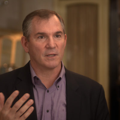 Frank Bruni, wearing a suit, gestures as he speaks.