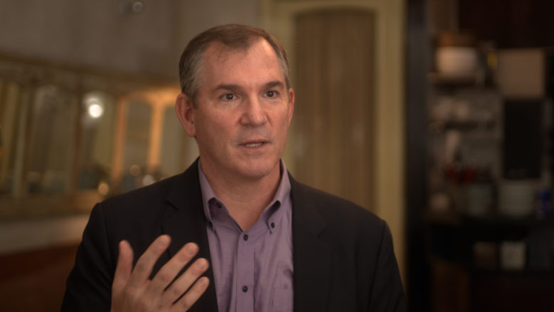 Frank Bruni, wearing a suit, gestures as he speaks.