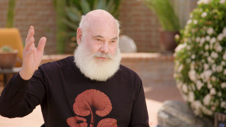 Dr Andrew Weil, wearing a black top with a red design, gestures with his hand as he speaks.